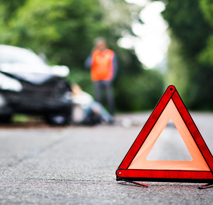 Warning triangle in foreground with aftermath of road traffic accident in the background